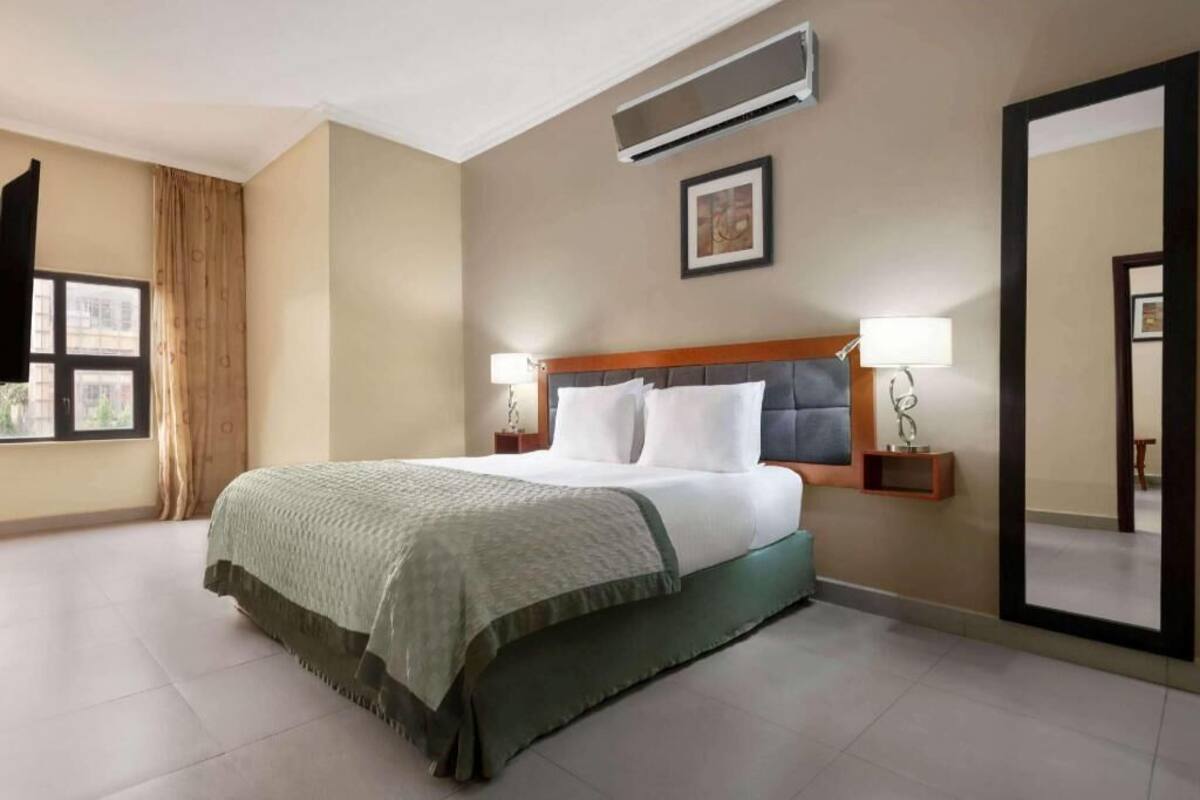 Een hotelkamer met een bed, twee bedlampen, een grote spiegel en een airconditioningsysteem.