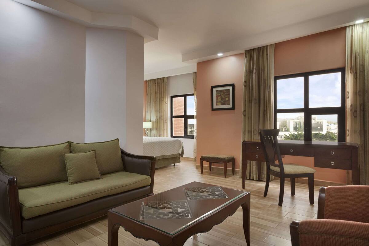 Un salon avec un canapé, une table basse, un bureau avec une chaise et un lit à l’arrière-plan.