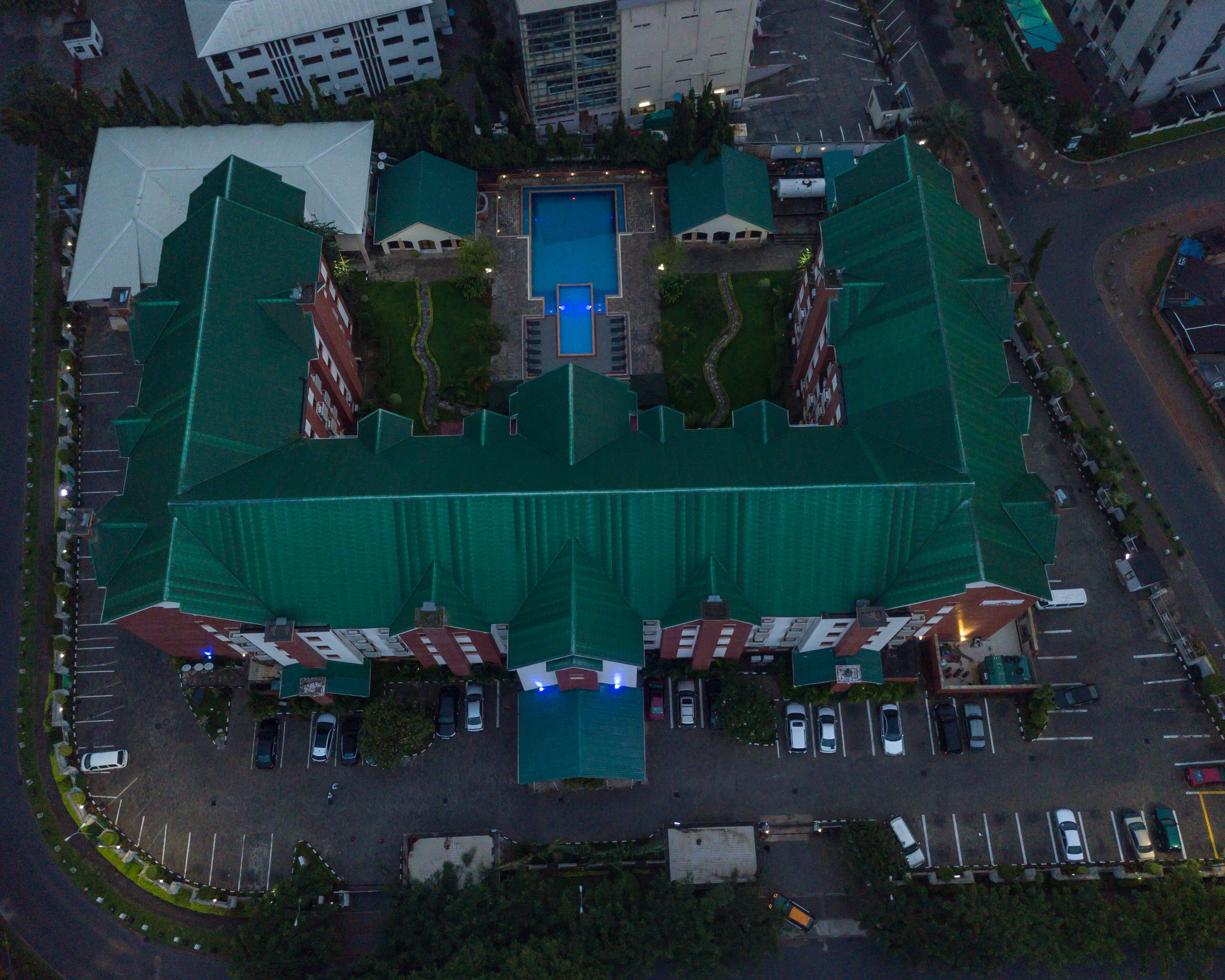 Vue aérienne d’un hôtel doté d’une piscine centrale, entouré d’un parking et d’un bâtiment dont le toit est végétalisé.
