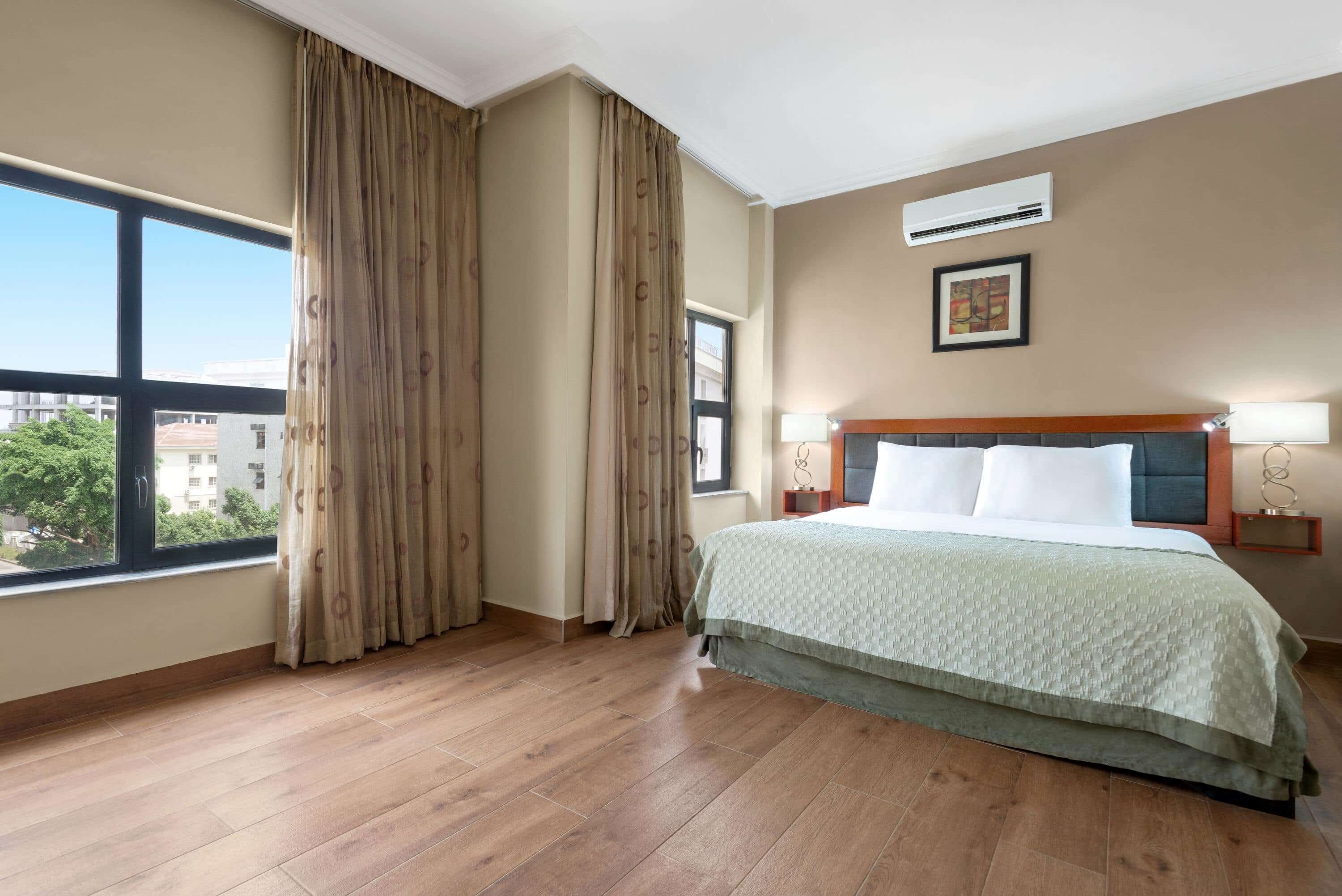 Habitación de hotel con un ventanal grande, cama con cabecero, equipo de aire acondicionado y un cuadro en la pared.