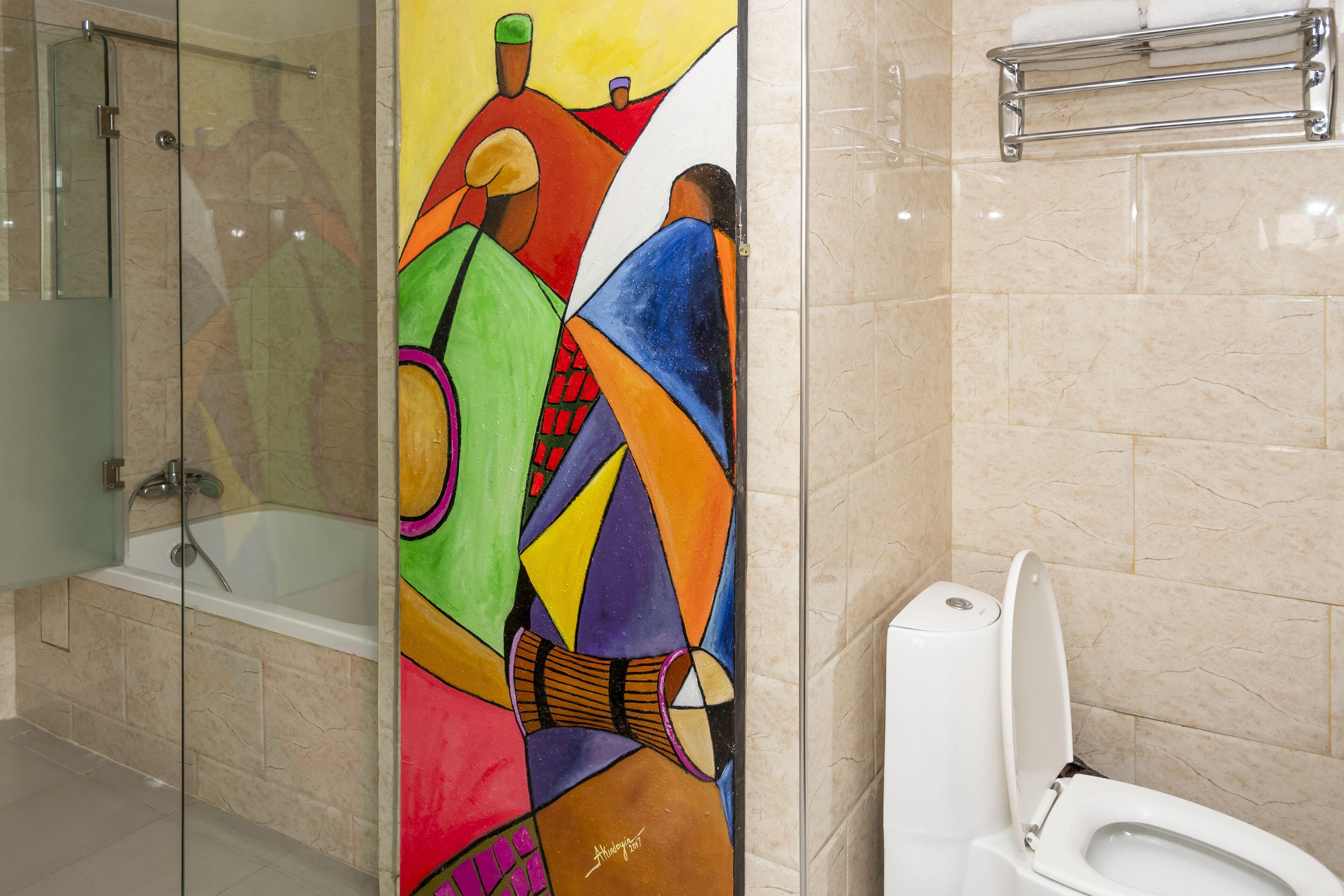 Un baño con cabina de ducha de vidrio, inodoro blanco y un mural abstracto y colorido en la pared.