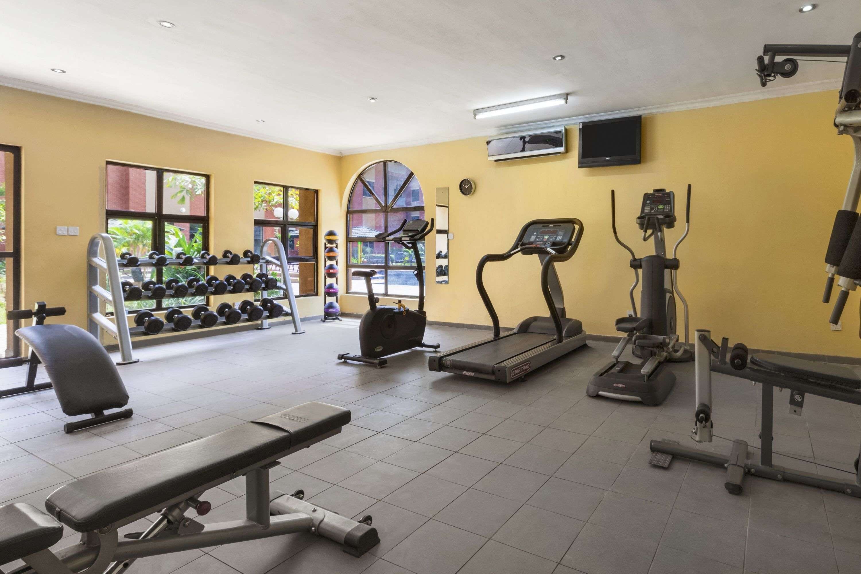 Une salle de sport équipée de tapis de course, de vélos elliptiques, d’haltères et de bancs.