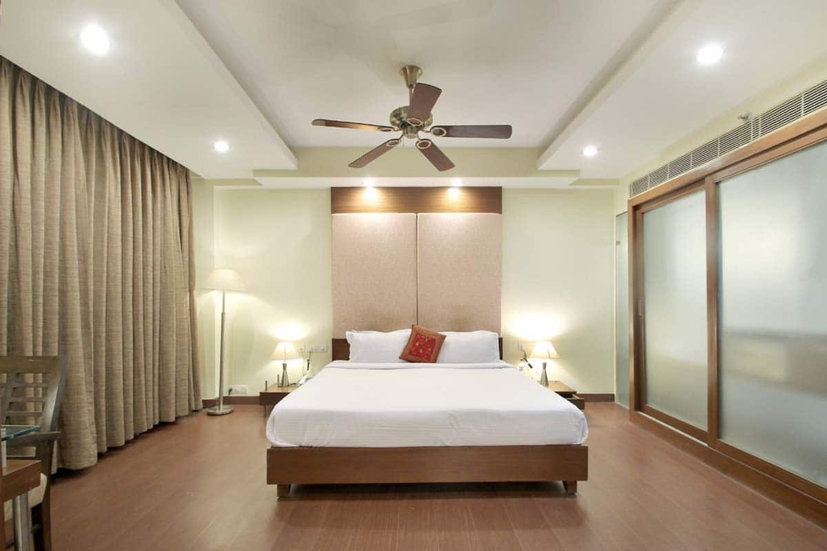 Ein Hotelzimmer mit einem großen Bett, einem Deckenventilator und Blick auf die Stadt durch ein großes Fenster.
