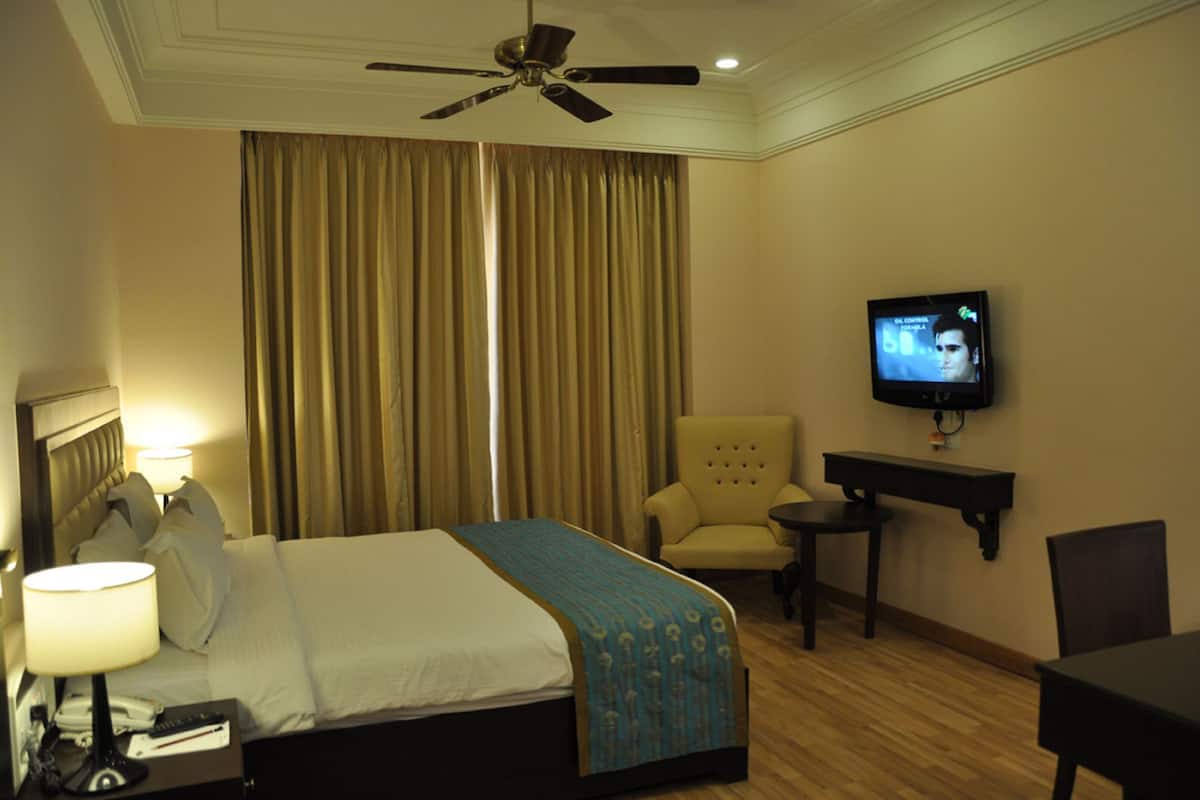 Ein Hotelzimmer mit Bett, Fernseher, Sessel und Schreibtisch.
