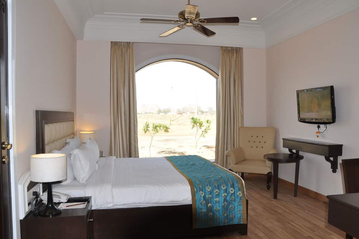 Ein Hotelzimmer mit Bett, Schreibtisch, Stuhl, Fernseher und Blick ins Freie.