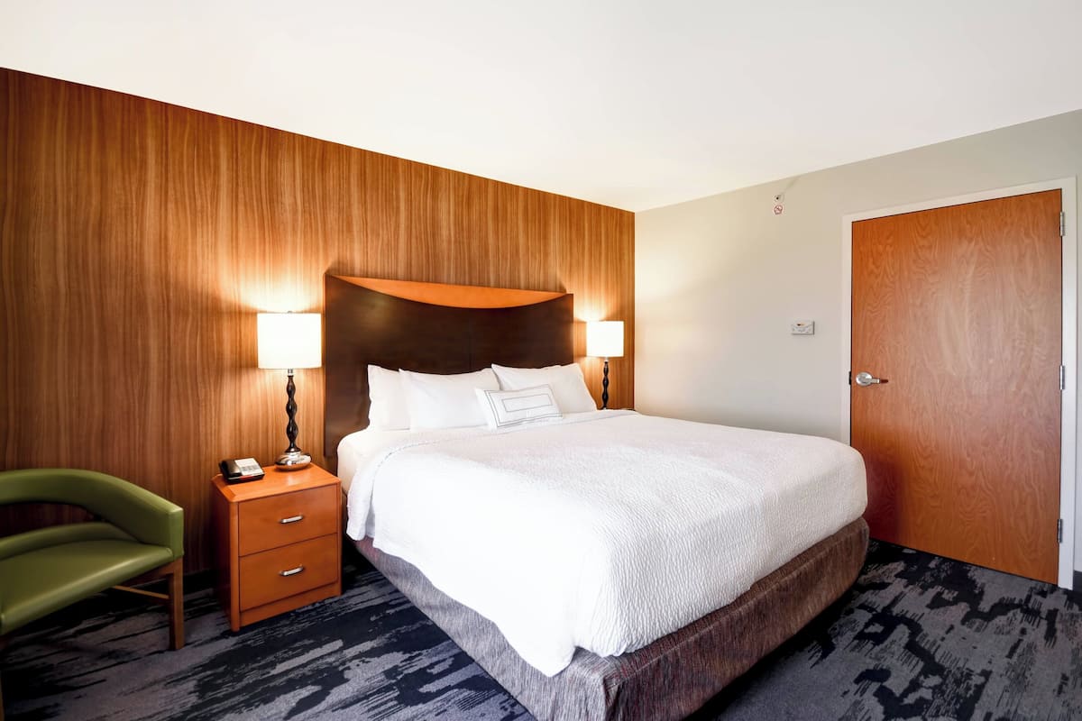 Ein Hotelzimmer mit einem großen Bett, zwei Nachttischlampen, einem Holzkopfschild, einem grünen Sessel, einem Nachttisch aus Holz und einer Tür.