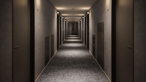 Un long couloir étroit, avec des portes des deux côtés, numérotées 201 et 212, et des luminaires encastrés le long du plafond.