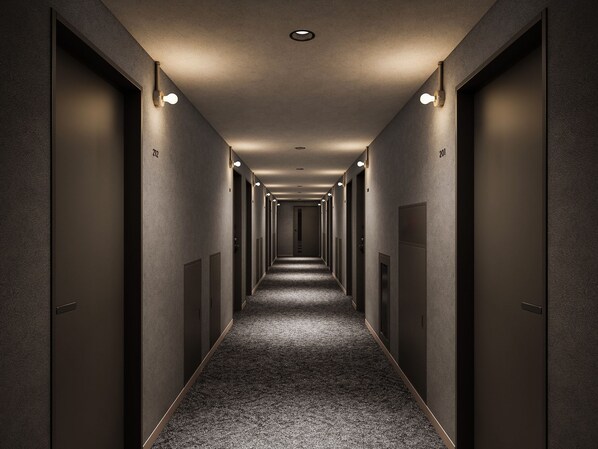 Un long couloir étroit, avec des portes des deux côtés, numérotées 201 et 212, et des luminaires encastrés le long du plafond.