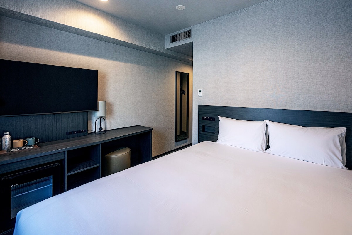 Une chambre d’hôtel avec un grand lit, un téléviseur à écran plat, un bureau avec une lampe et un miroir.
