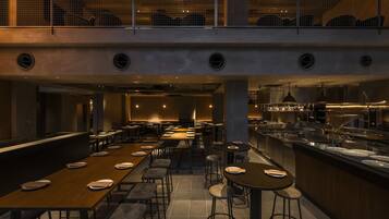 A modern restaurant with multiple dining tables and stools, a kitchen area, and a mezzanine level.