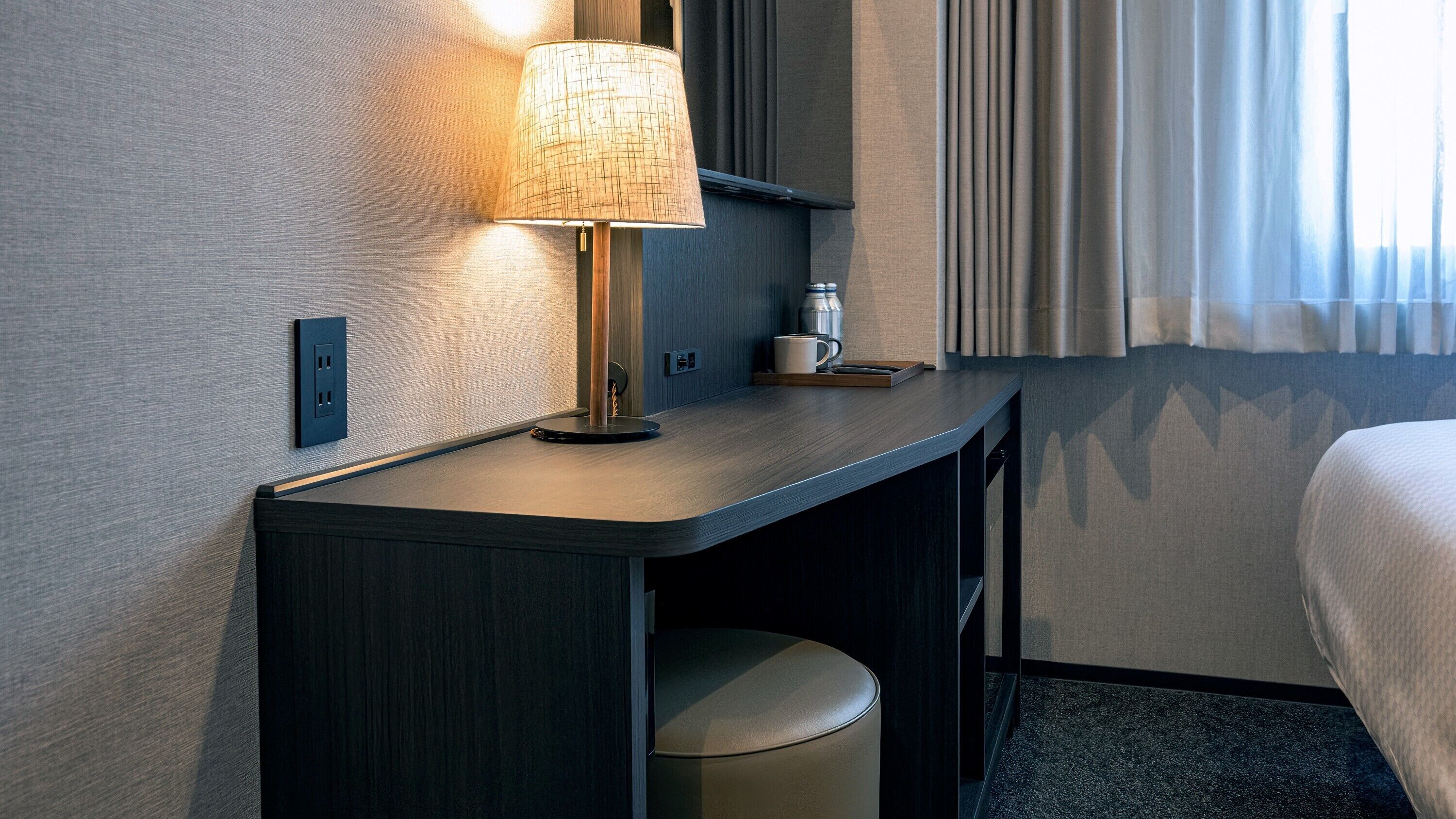 Ein Hotelzimmer mit Schreibtisch, Lampe, Tasse und Papierkorb.