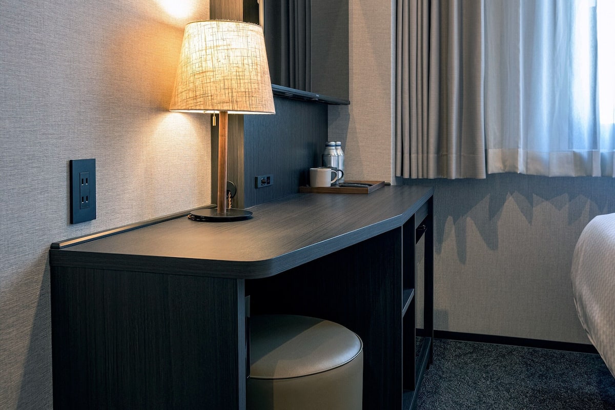 Une chambre d’hôtel équipée d’un bureau, d’une lampe, d’une tasse et d’une poubelle.