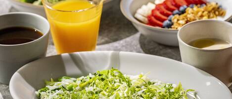 A breakfast setting with various dishes including a plate of rice with greens, a bowl of fruit, and a glass of orange juice.