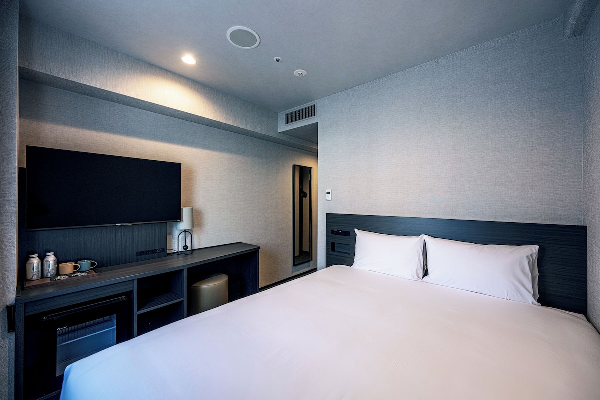 Une chambre d’hôtel avec un grand lit, un téléviseur à écran plat, un bureau avec une lampe et un miroir.