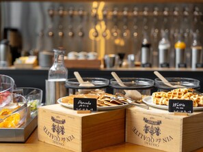 Ein Frühstücksbuffet mit beschrifteten Behältern für Pfannkuchen und Waffeln, sowie Holzkisten mit dem Namen des Hotels.