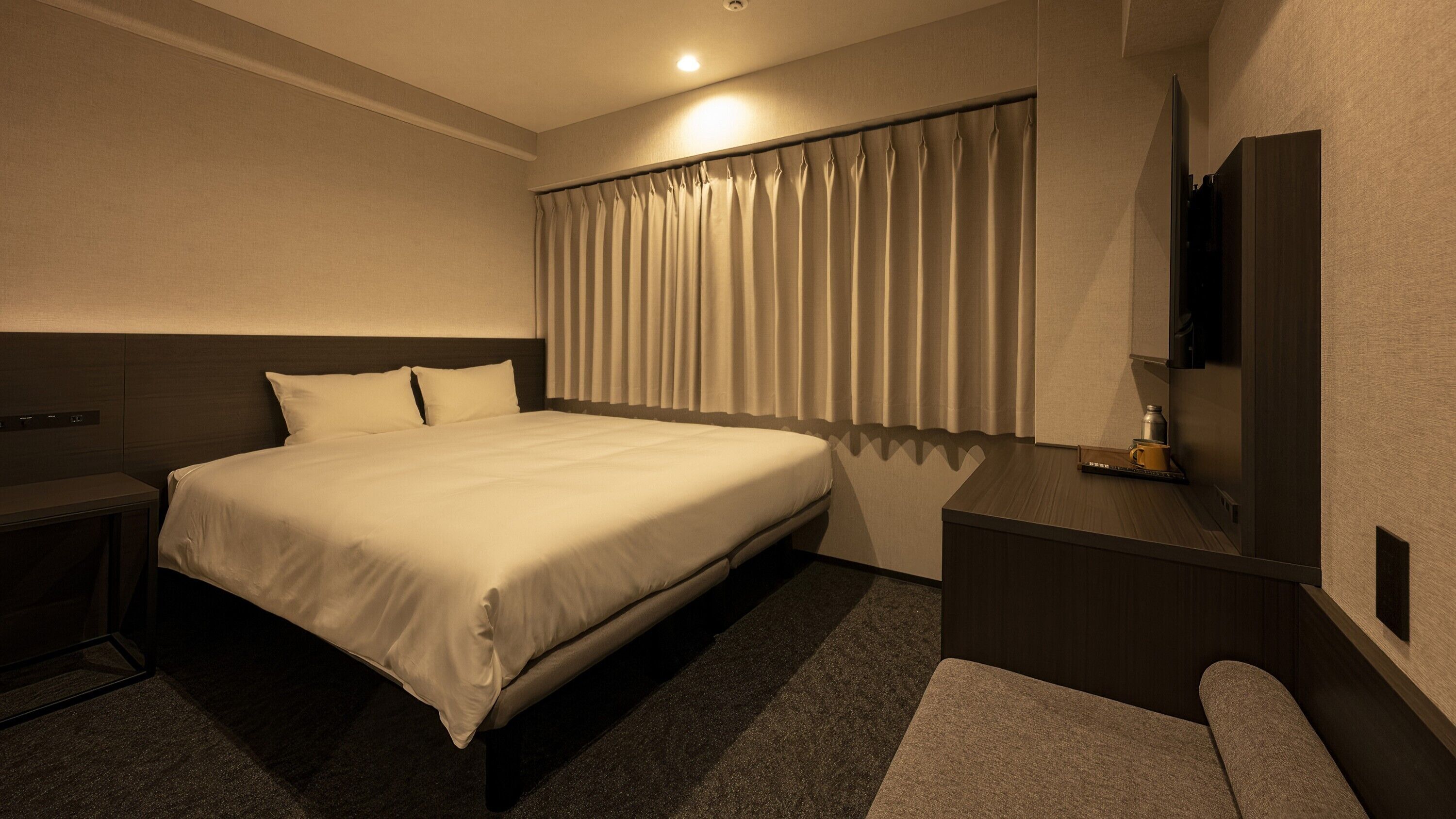 Ein Hotelzimmer mit Bett, Nachttisch, Schreibtisch, Spiegel und einem Fenster mit Vorhängen.