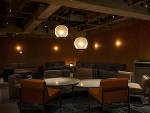 Ein moderner Lounge-Bereich mit runden Tischen, Sofas und hängenden, kugelförmigen Lampen.