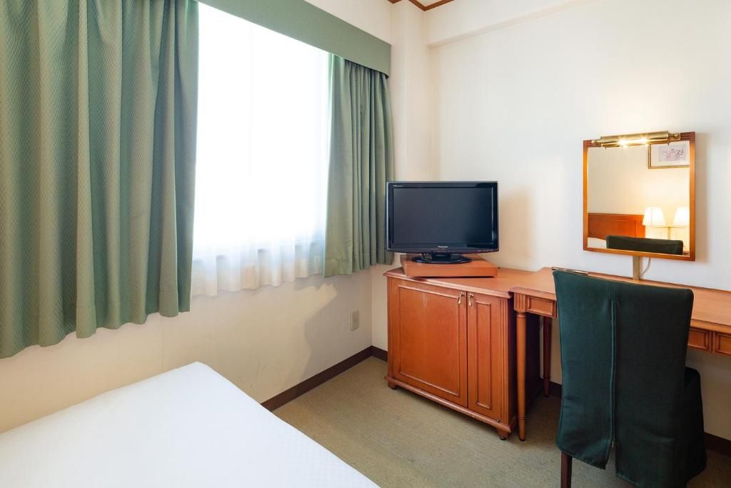 A hotel room with a bed, a desk with a television, a mirror, and a chair.