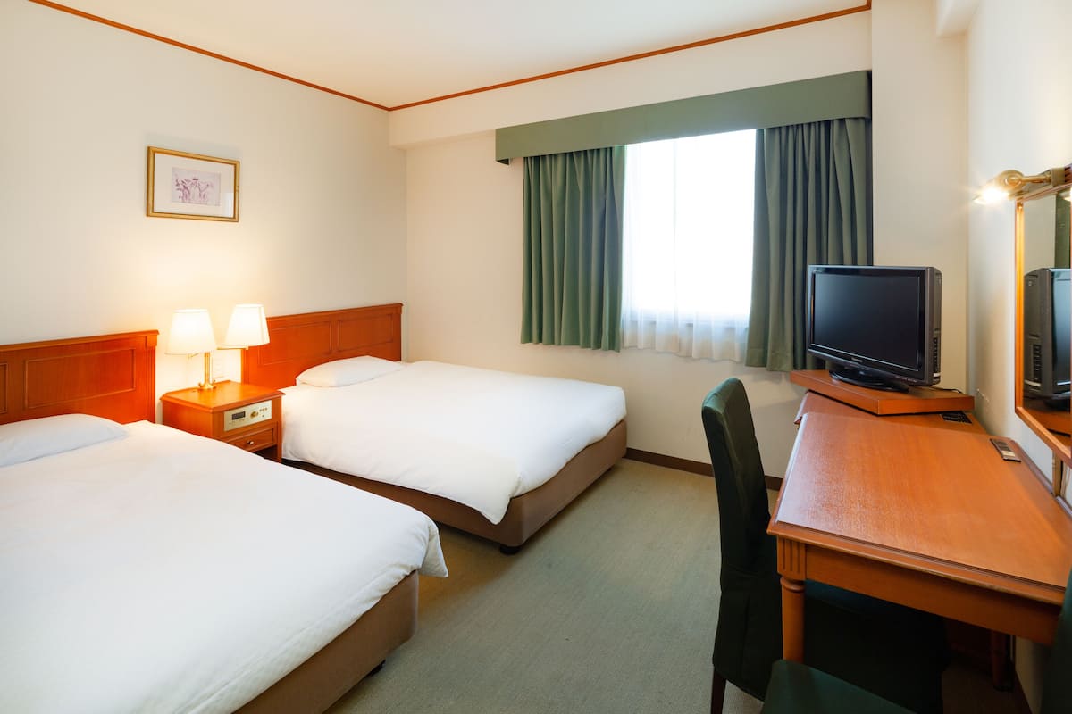 Une chambre d’hôtel avec deux lits, un bureau avec une télévision et une chaise.