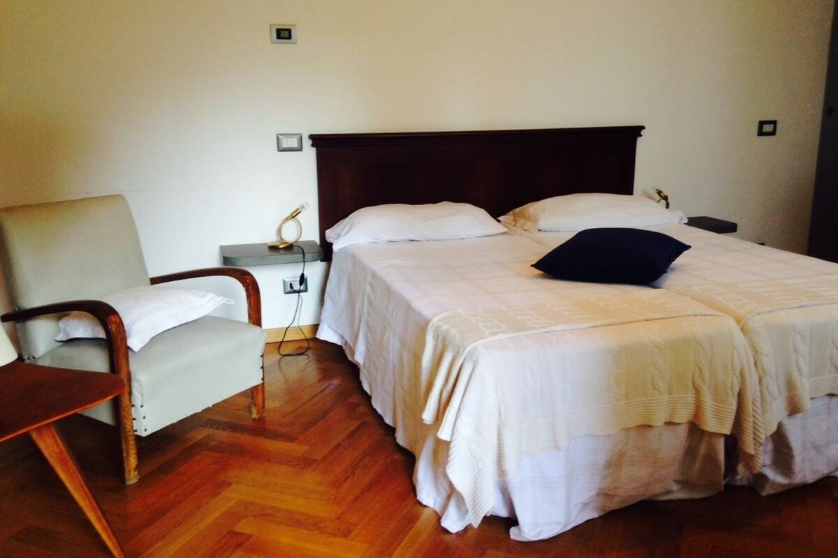 A bedroom with a double bed, a bedside table, a chair, and a wooden floor.