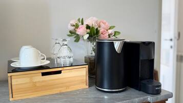 Eine Küchenarbeitsplatte mit einer Kaffeemaschine, einem Glasbehälter, einer weißen Tasse und einer Vase mit rosa Blumen.