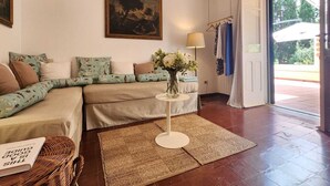A cozy living room with a sofa, a small table with a lamp, a painting on the wall, and a view through a door. - Don Gaspano  (Pace del Mela)