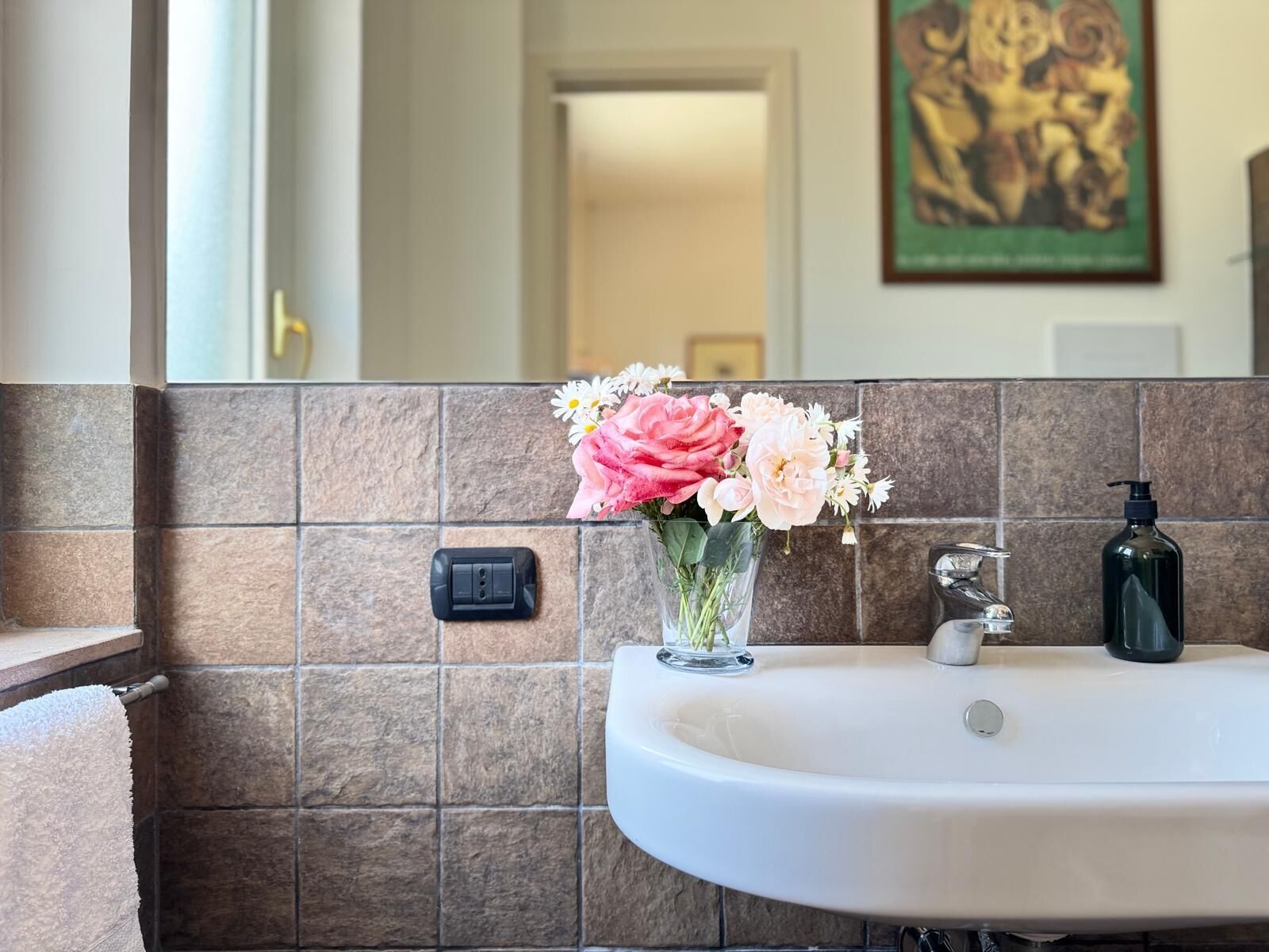 A bathroom with a white sink, a hand dryer, and a vase of flowers on the wall.