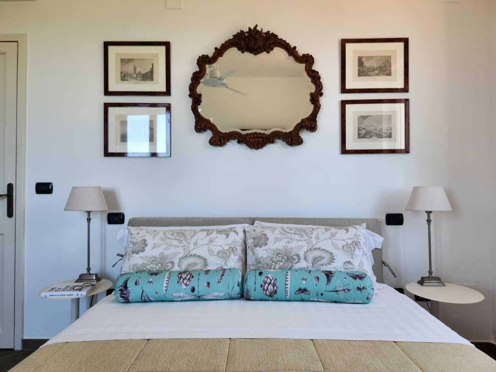 Une chambre d’hôtel avec un grand lit, deux tables de chevet avec des lampes, un miroir et des tableaux encadrés au mur.