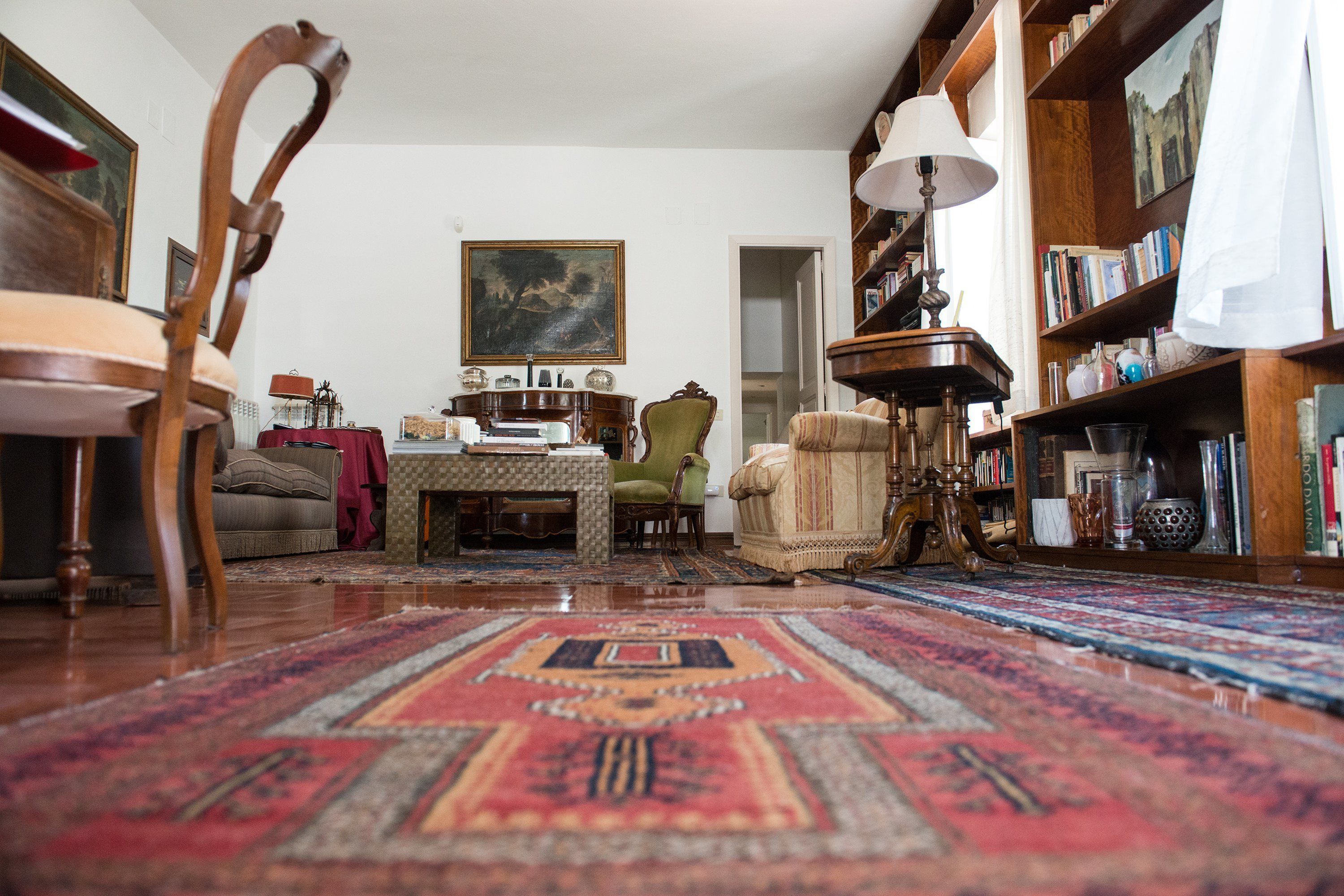 A cozy living room with a large rug, wooden furniture, a bookshelf, and a painting on the wall.