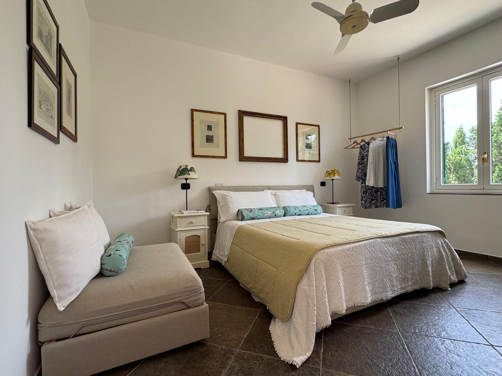 Un dormitorio con cama, mesitas de noche, cómoda y ventana con vistas a árboles.