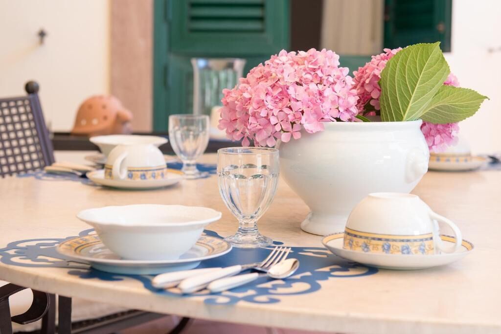 A table set with white and blue patterned tableware, a clear glass, and a vase with pink flowers.