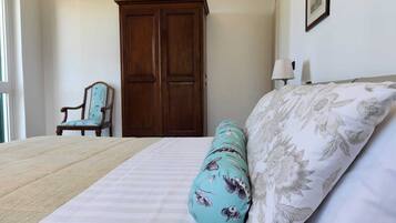 A bedroom with a large bed, a wooden wardrobe, a chair, and a wall-mounted lamp.