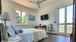 A bedroom with a bed, a desk, a chair, a TV, and a window. - Don Gaspano  (Pace del Mela)