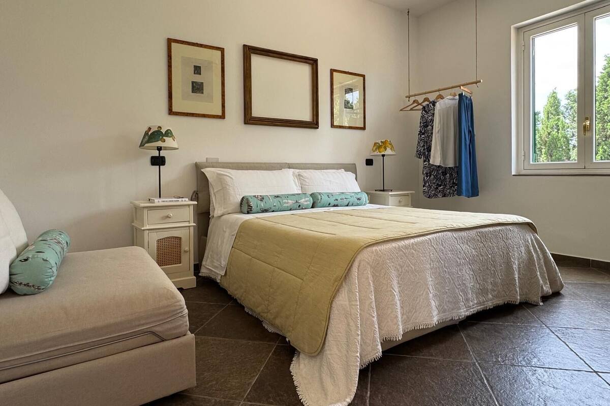 A bedroom with a bed, a nightstand, a dresser, a chair, a window, and a door.
