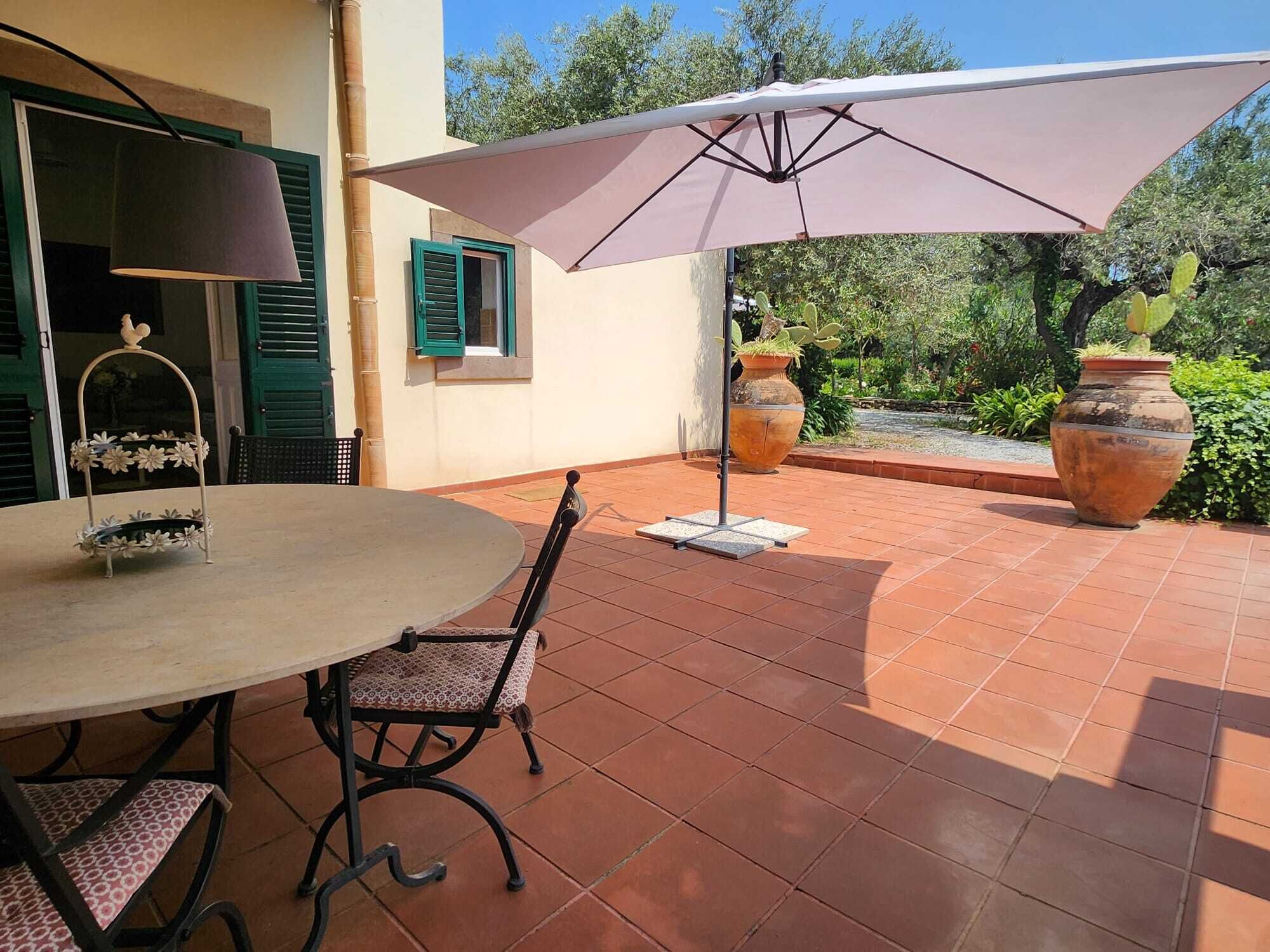 Un patio al aire libre con una mesa redonda, sillas y una sombrilla grande.