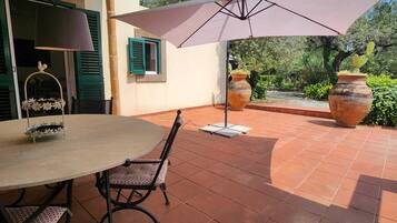 Un patio al aire libre con una mesa redonda, sillas y una sombrilla grande.