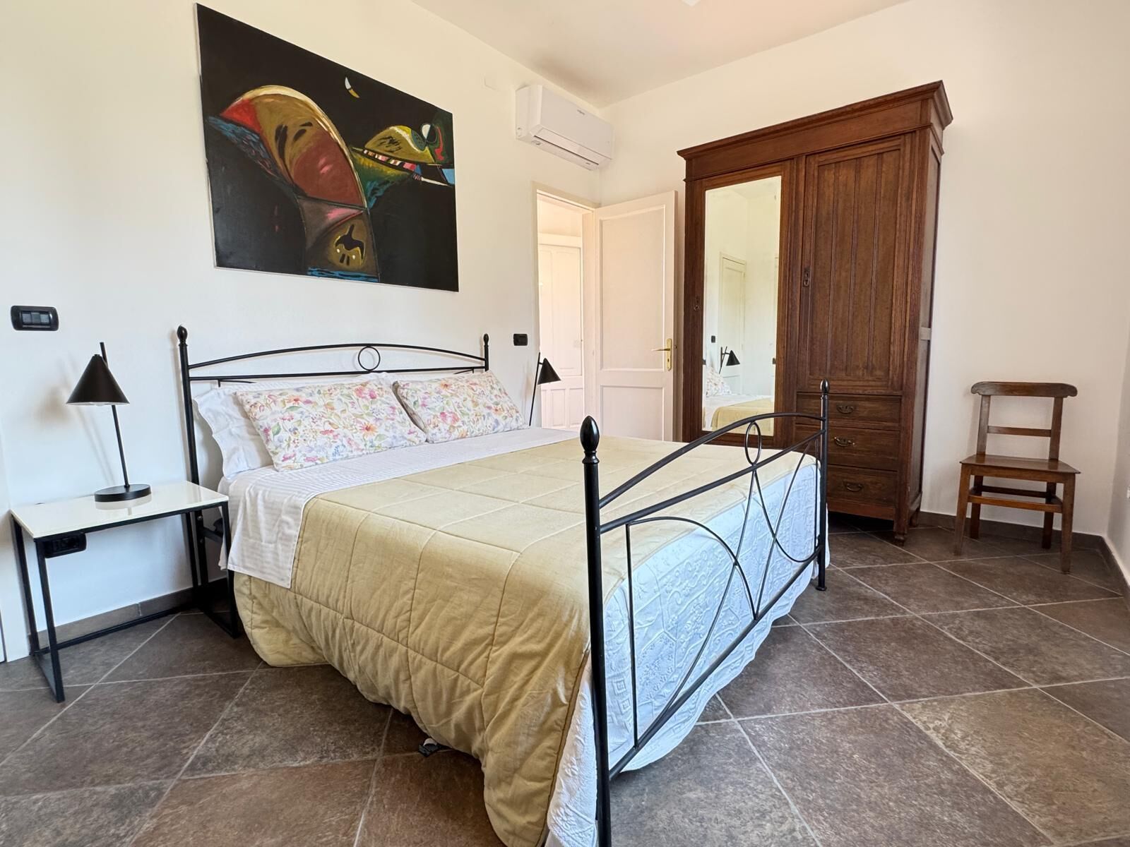 A bedroom with a bed, a nightstand, a chair, a wardrobe, and a painting on the wall.