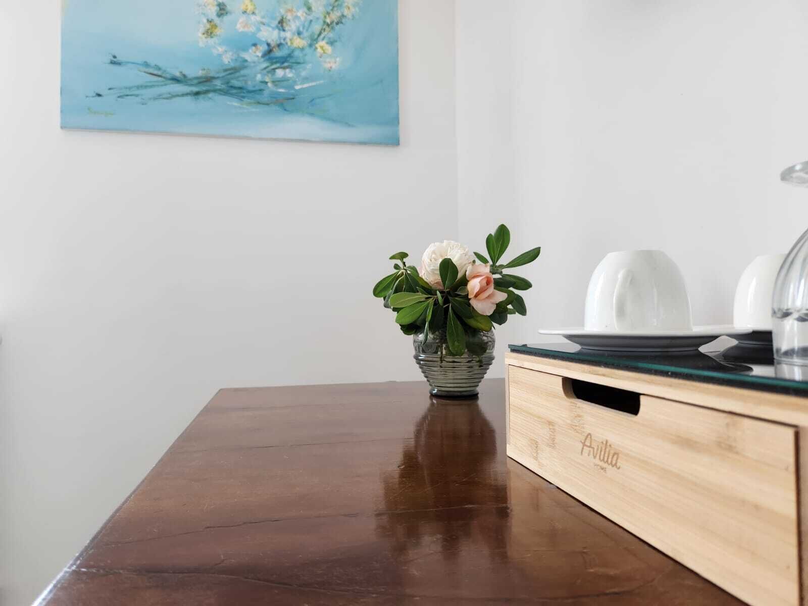 Une table en bois sur laquelle se trouvent un vase en verre contenant des fleurs, une assiette blanche et un récipient en verre, le tout posé sur un meuble en bois.