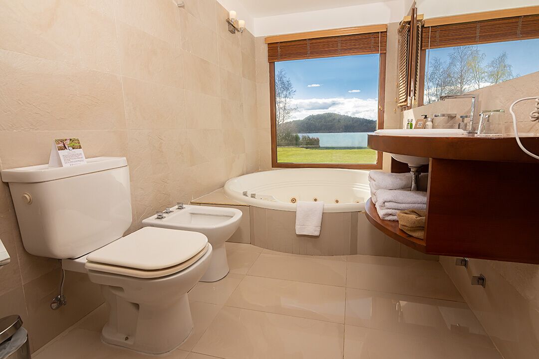 A bathroom with a toilet, bidet, and a large bathtub with a view of a lake and mountains.