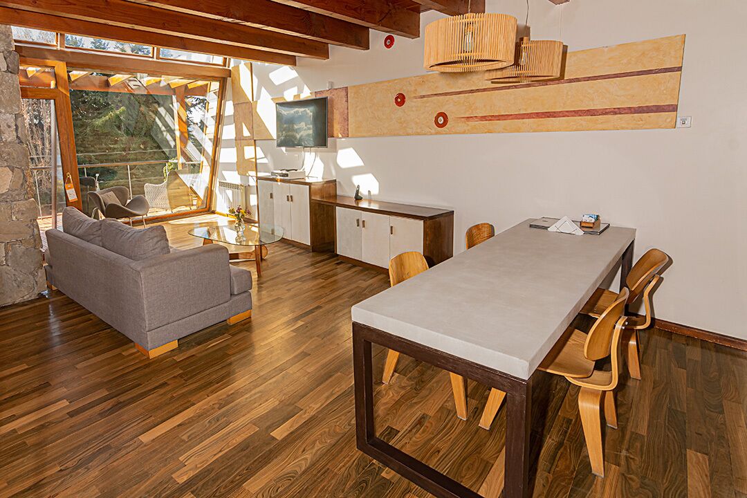 Una sala de estar moderna con un sofá, una mesa de comedor y sillas. Hay un televisor sobre un mueble de madera y un ventanal que proporciona luz natural.