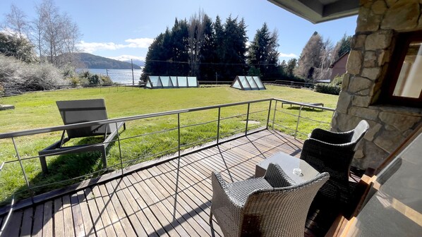 A deck with wicker chairs and a view of a lake and forest.