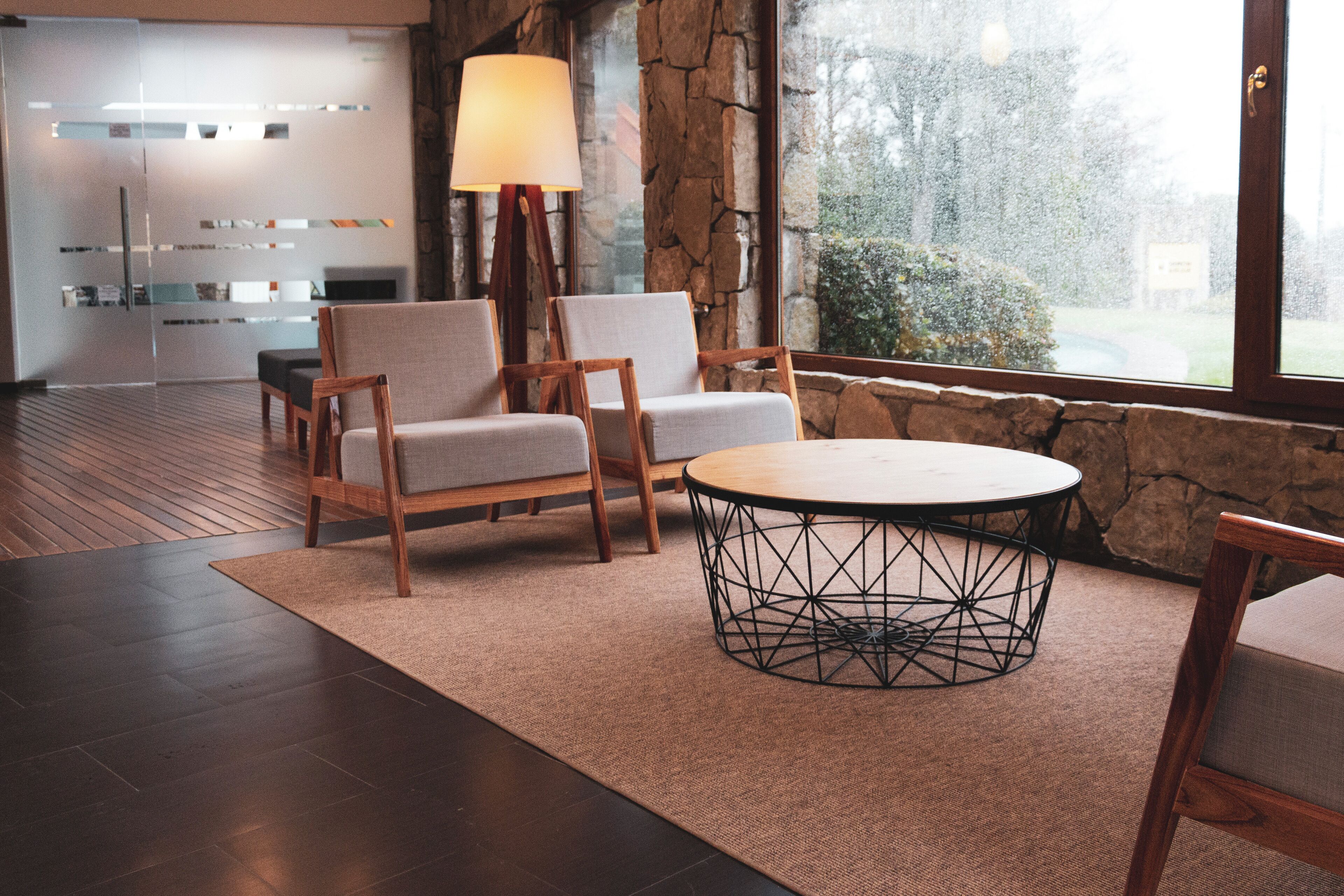 Um interior moderno com parede de pedra, uma mesa redonda com base metálica geométrica e duas cadeiras estofadas.