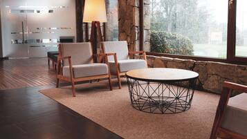 Um interior moderno com parede de pedra, uma mesa redonda com base metálica geométrica e duas cadeiras estofadas.