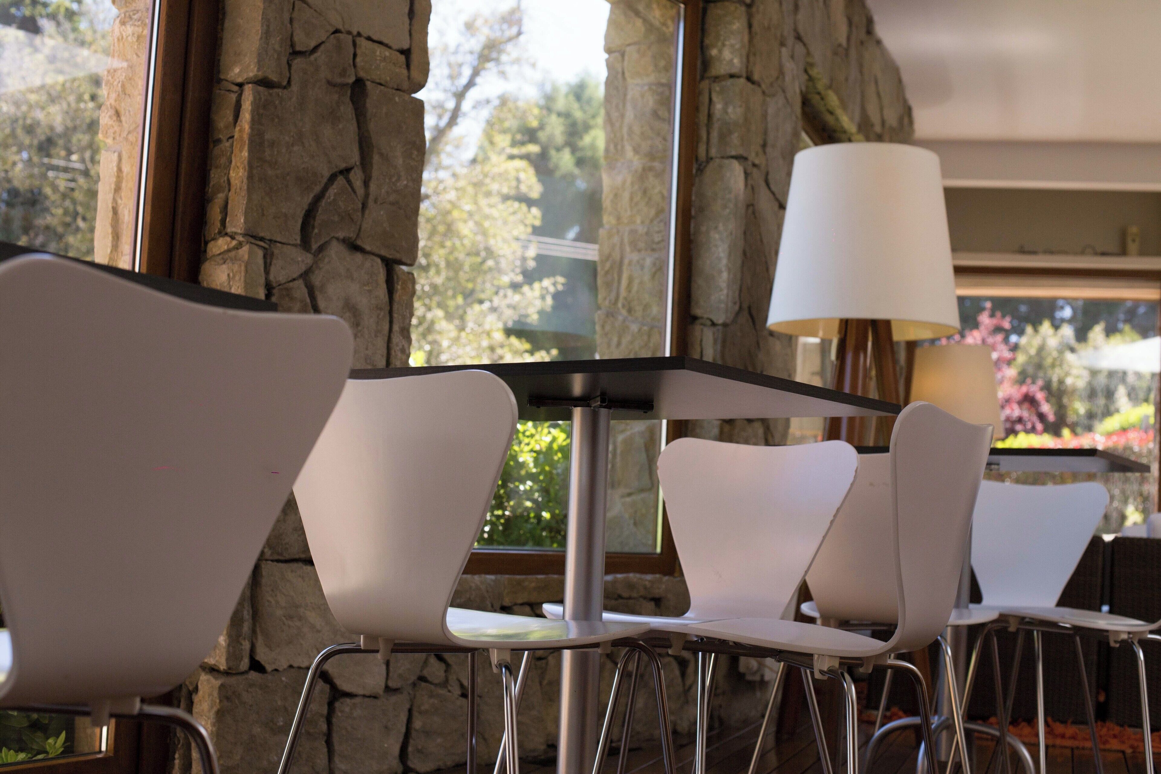 A dining area with white chairs and a table, stone walls, and a window with a view of trees and flowers.