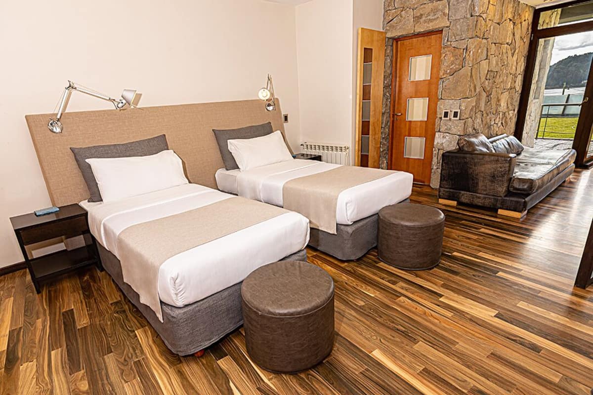 Camera d'albergo con due letti, un muro in pietra, pavimento in legno, un divano e vista su un lago.