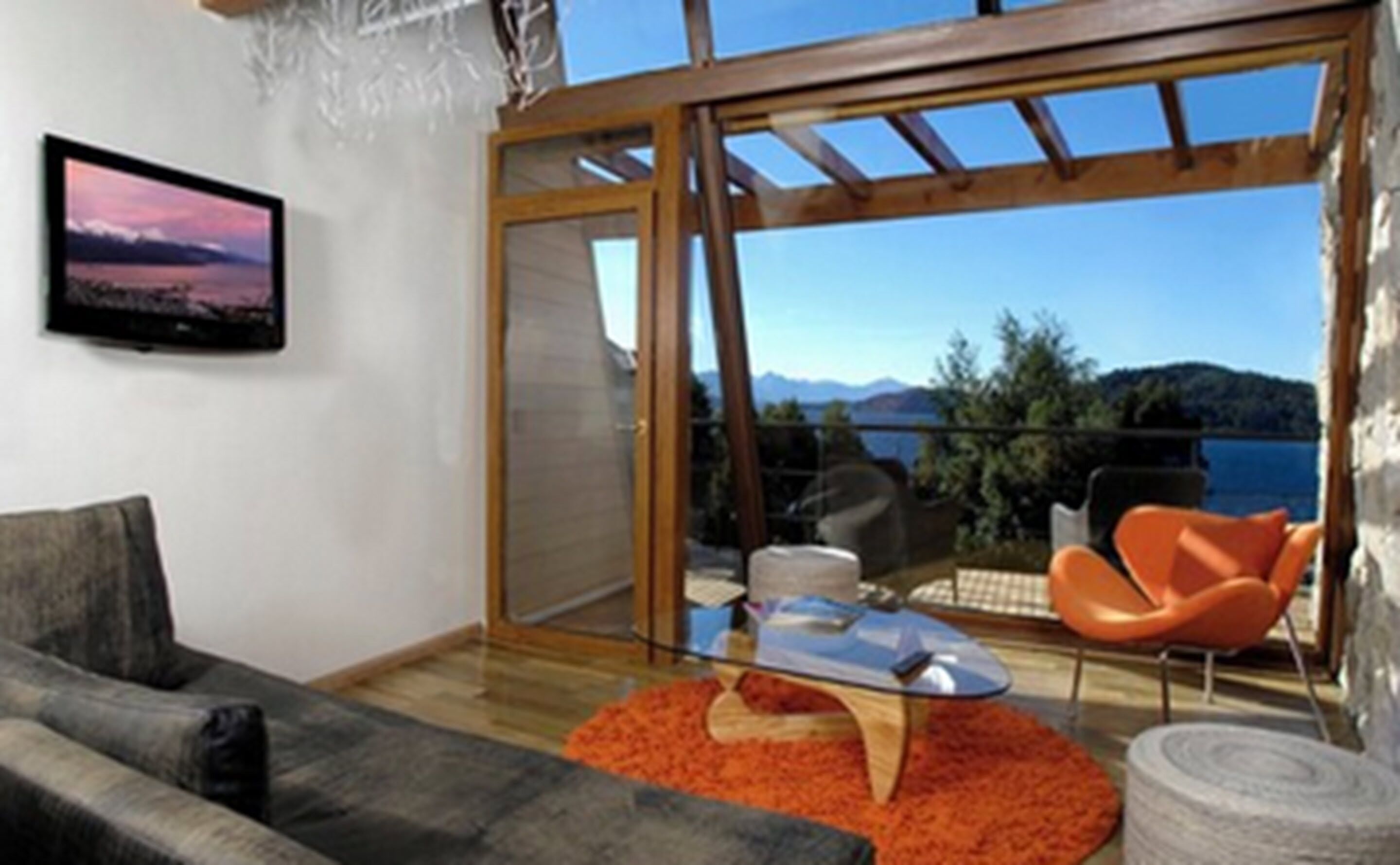 Ein modernes Wohnzimmer mit einer Couch, einem Couchtisch und Blick auf einen See und Berge durch große Glaswände.