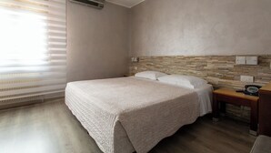 Een slaapkamer met een groot bed, een houten nachtkastje, een telefoon en een wand met een steenmotief.