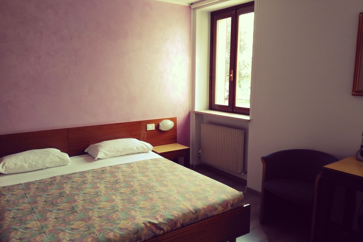 A hotel room with a bed, a window, a radiator, and a desk.