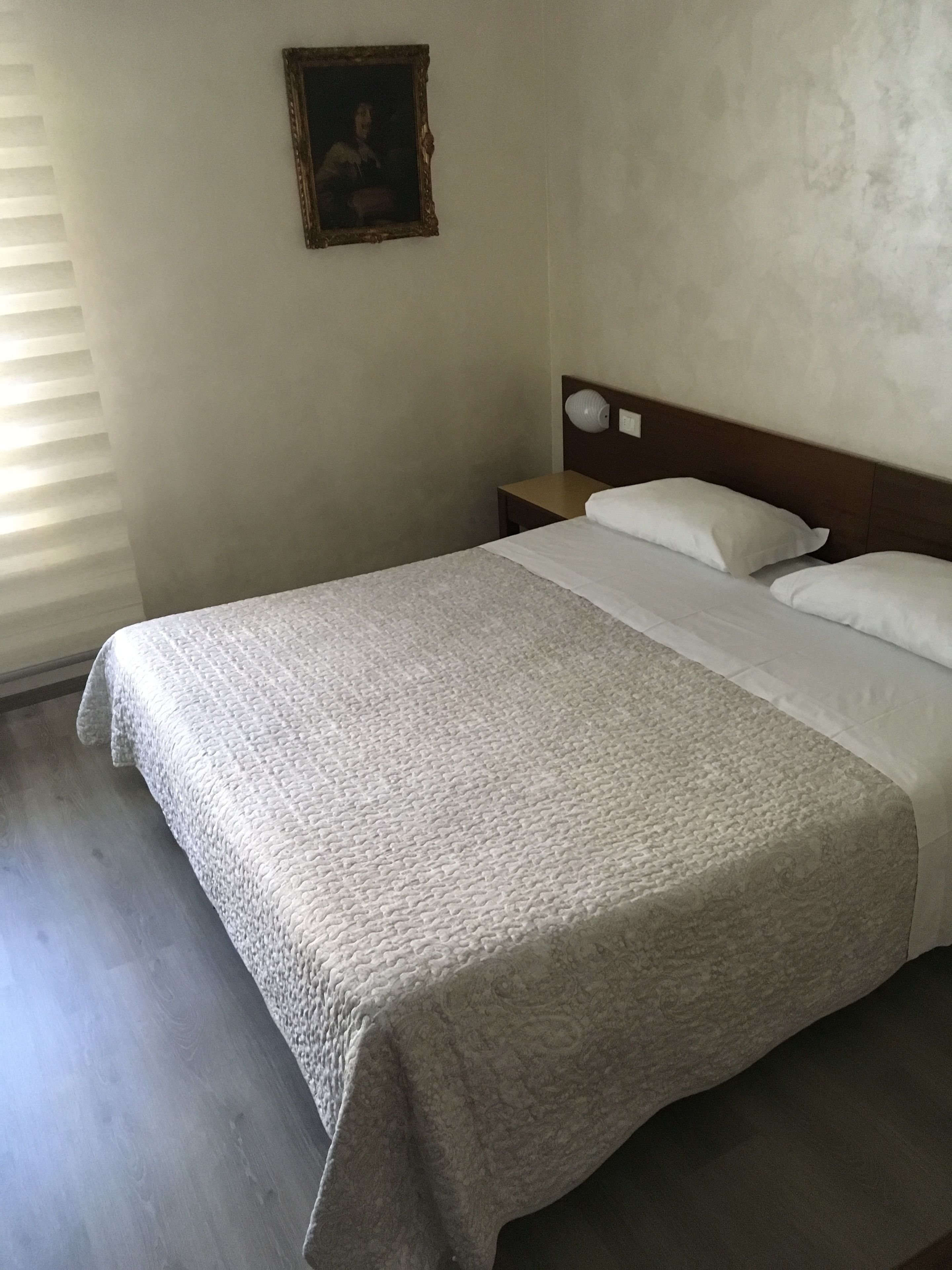 Ein ordentlich bezogenes Bett mit einer gemusterten Decke, ein hölzernes Kopfteil, ein Nachttisch mit einer Lampe und ein gerahmtes Bild an der Wand.