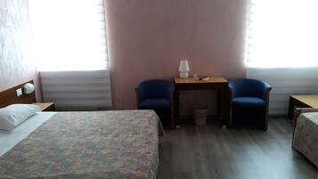 A hotel room with a bed, two chairs, a small table with a lamp, and a waste bin.
